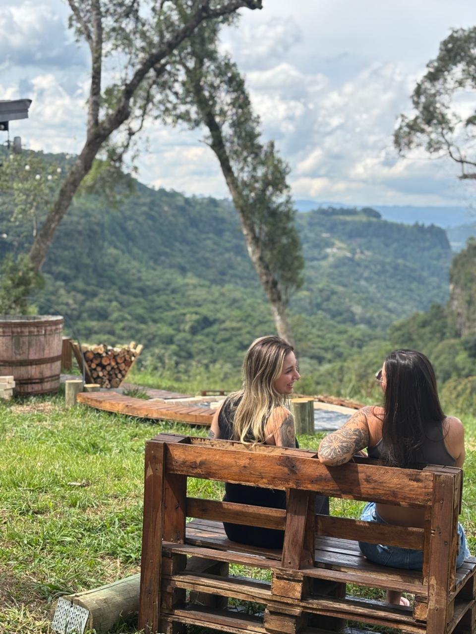 Amigas conversando em banco de madeira com vista para as montanhas